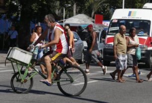 Calor em Bangu | homem de bicicleta vestido com a camisa do bangu atravessa rua sob forte sol e calor